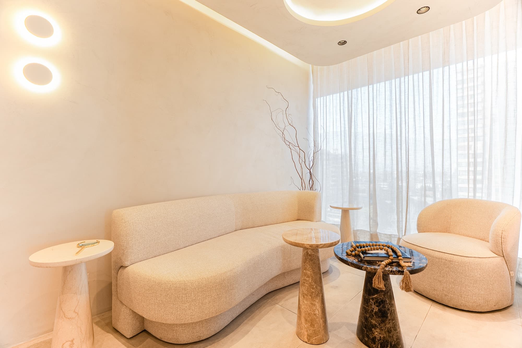 Waiting lounge with curved sofa, marble tables, and sheer curtains